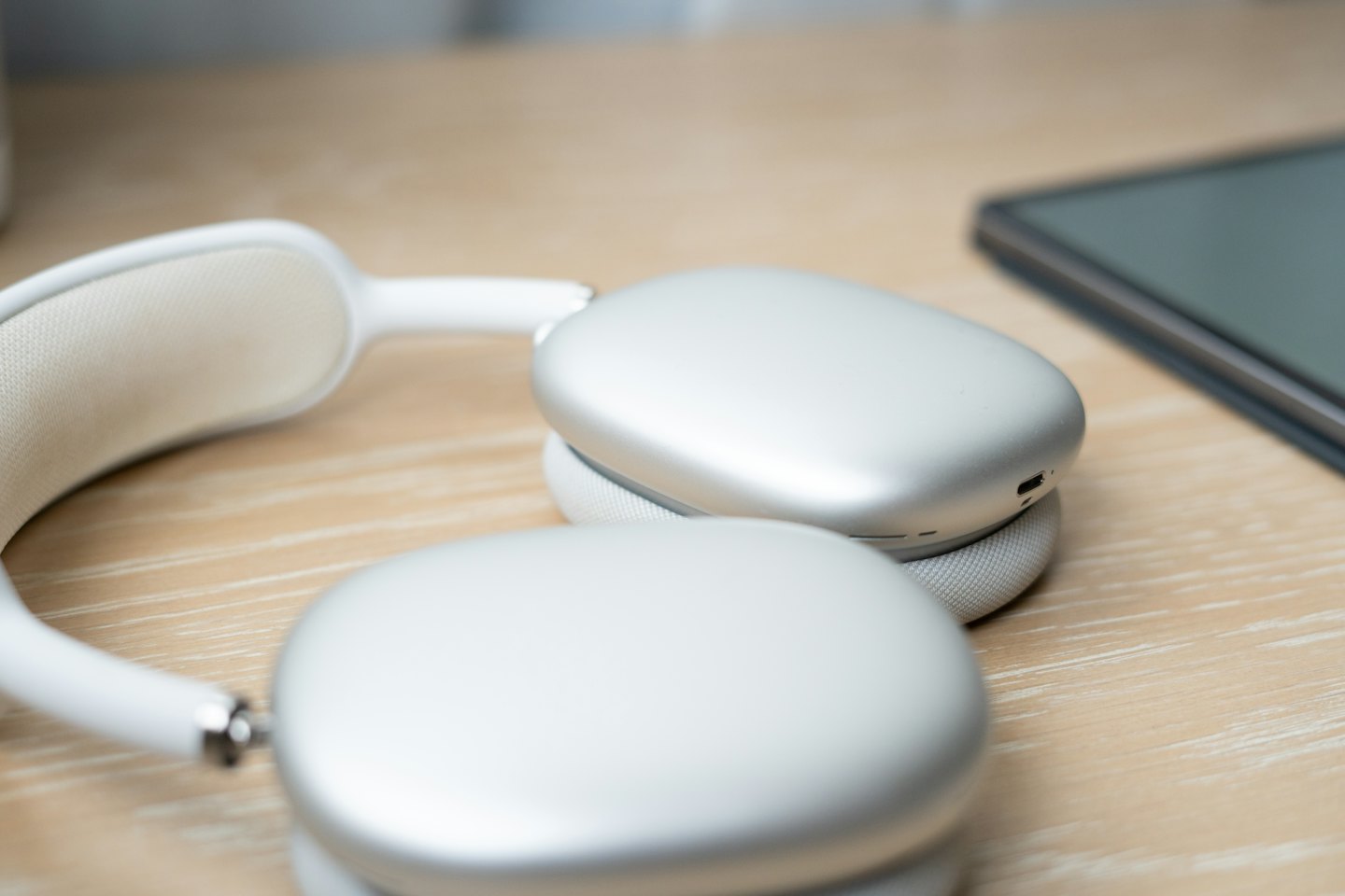 Silver and white wireless headphones on a wooden desk.